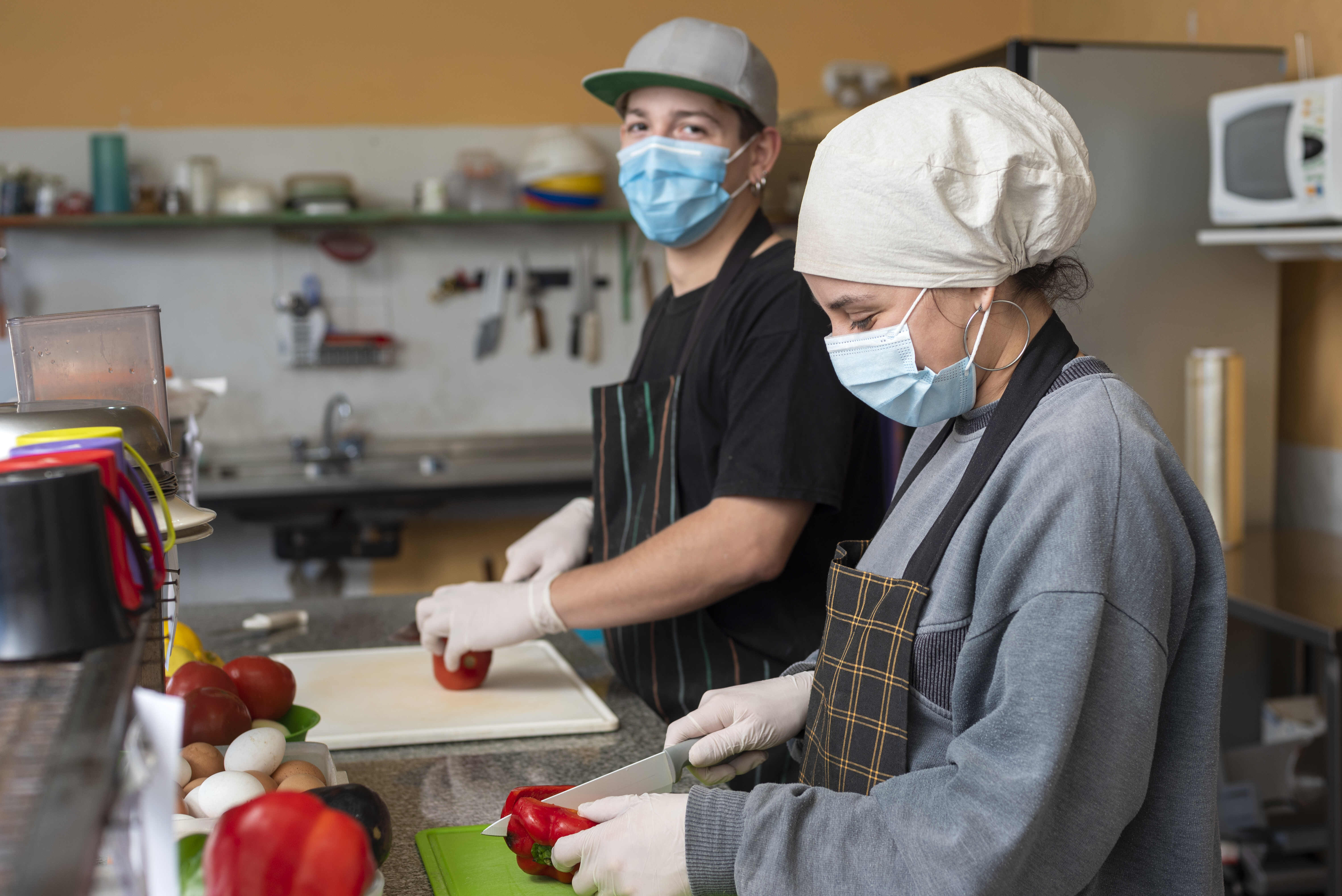 The two young chefs slicing vegetables wearing medical masks